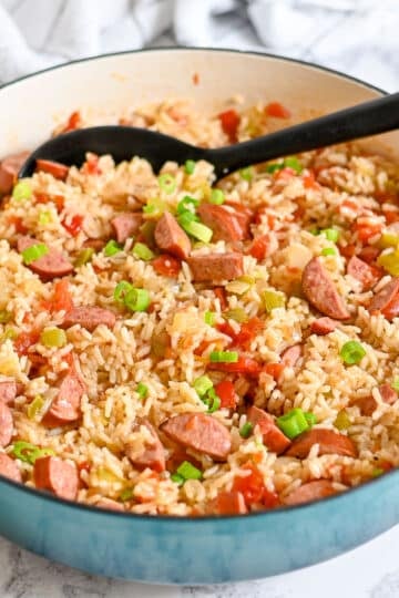A skillet filled with sausage and rice, mixed with bell peppers and topped with chopped green onions.