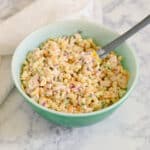 A green bowl filled with creamy Rotisserie Chicken Macaroni Salad and a spoon, set on a marble surface.