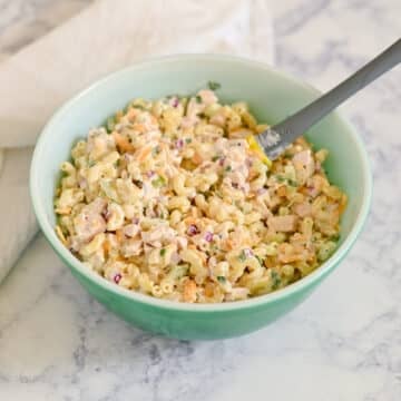 A green bowl filled with creamy Rotisserie Chicken Macaroni Salad and a spoon, set on a marble surface.