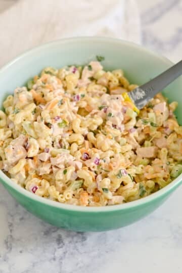 A green bowl filled with creamy Rotisserie Chicken Macaroni Salad and a spoon, set on a marble surface.
