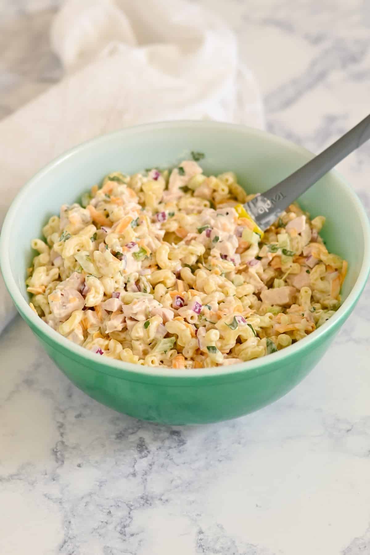 A green bowl filled with creamy rotisserie chicken macaroni salad with veggies sits on a marble countertop.
