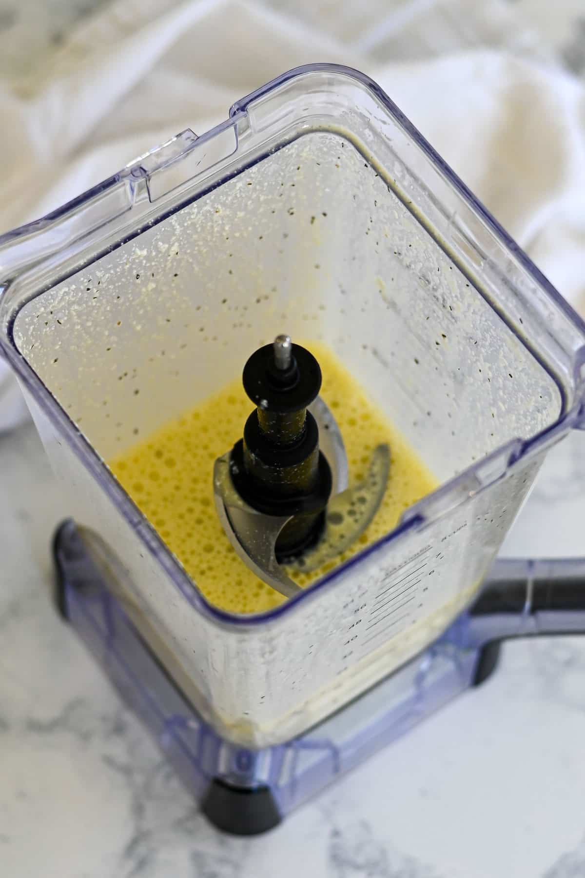 Blender with a yellow liquid mixture inside-perfect for making Spinach Egg Cups-photographed from above on a marble countertop.