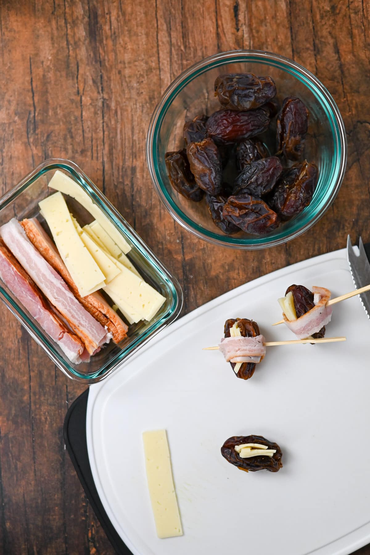 Cheese Stuffed Dates Wrapped in Bacon make a delicious appetizer, featuring dates and cheese on a table, with some dates stuffed and wrapped in bacon, all beautifully arranged on a white cutting board.