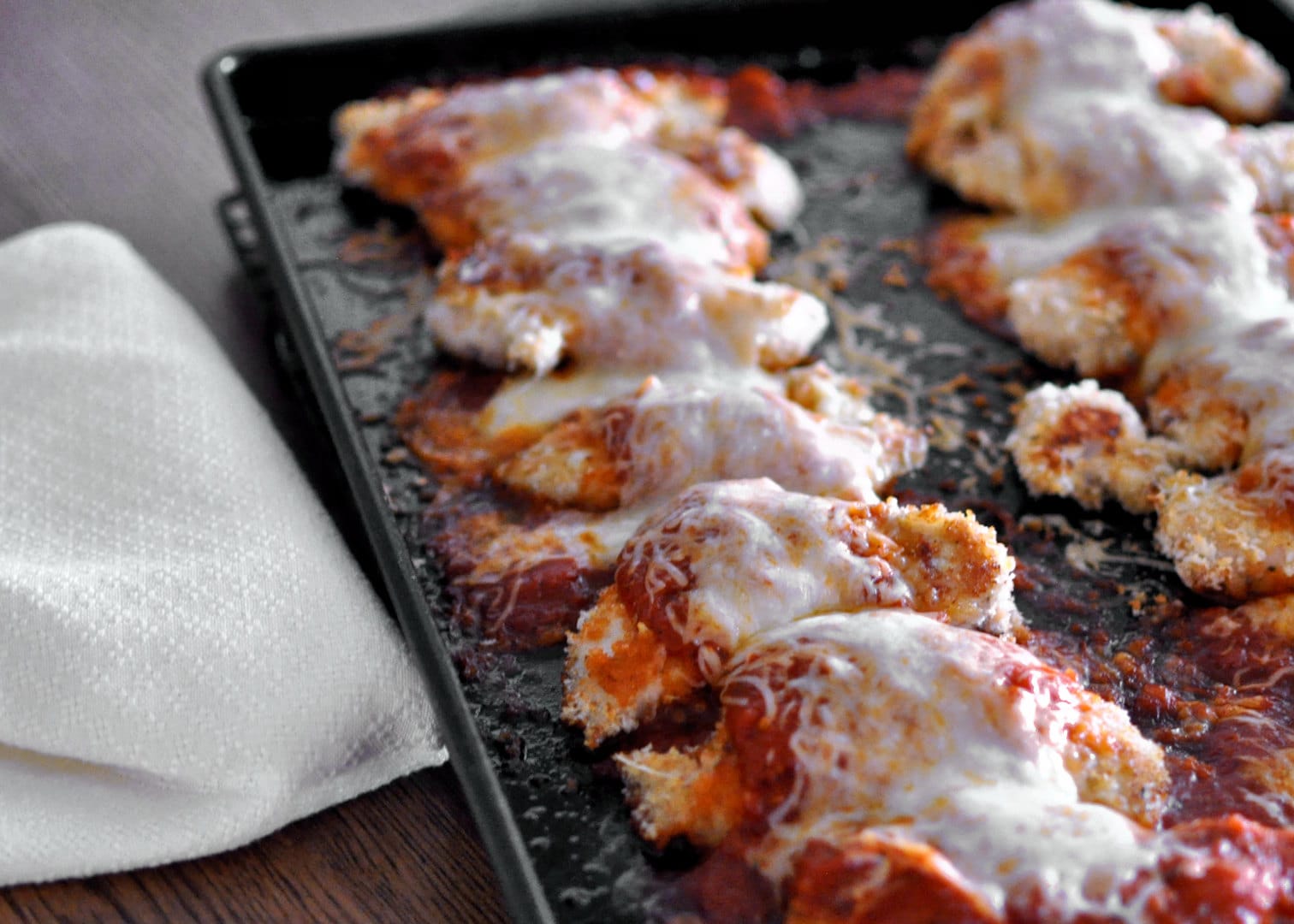 Easy Baked Chicken Parmesan just baked still on dark baking pan