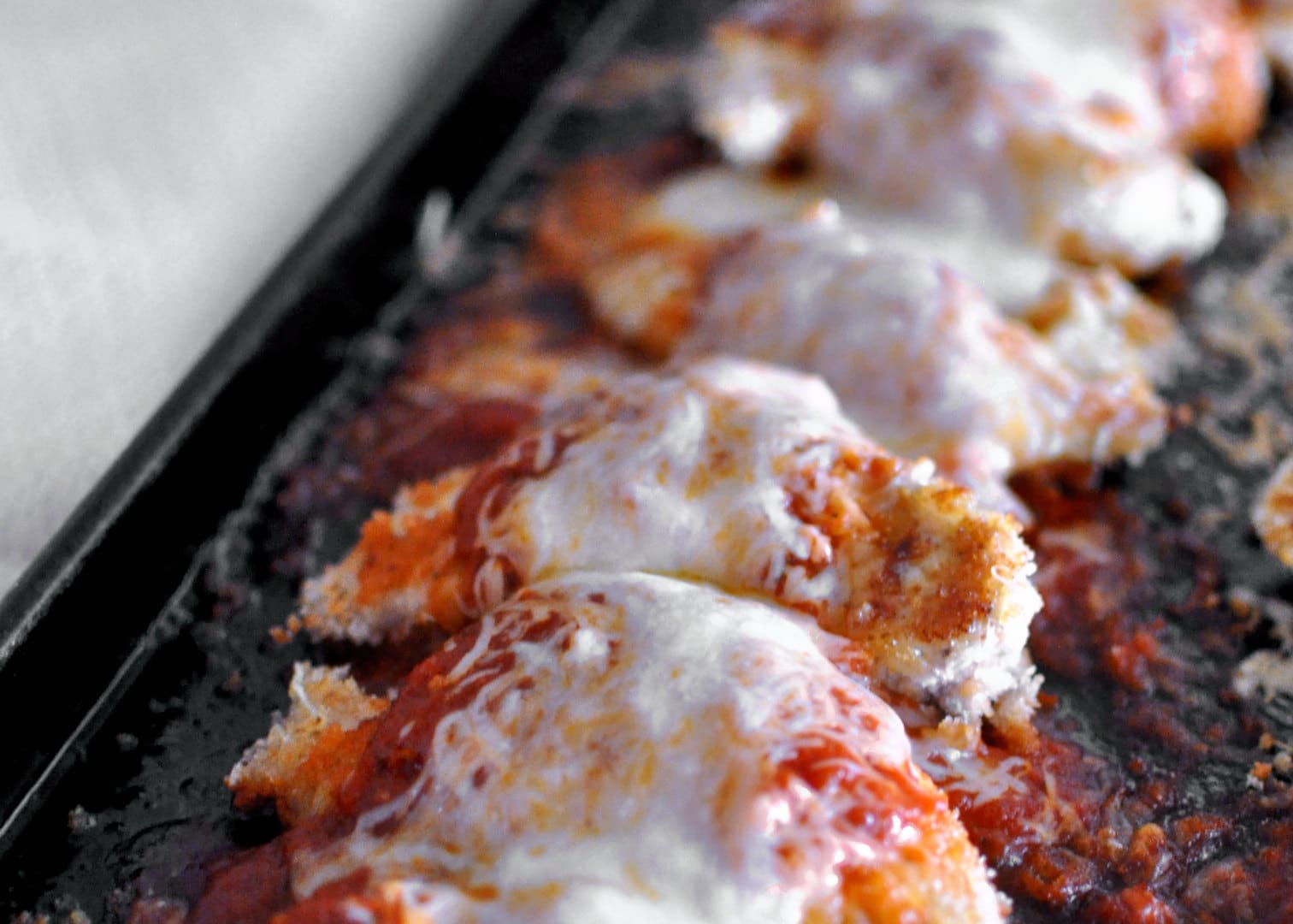 chicken with tomato sauce and cheese on a dark baking sheet