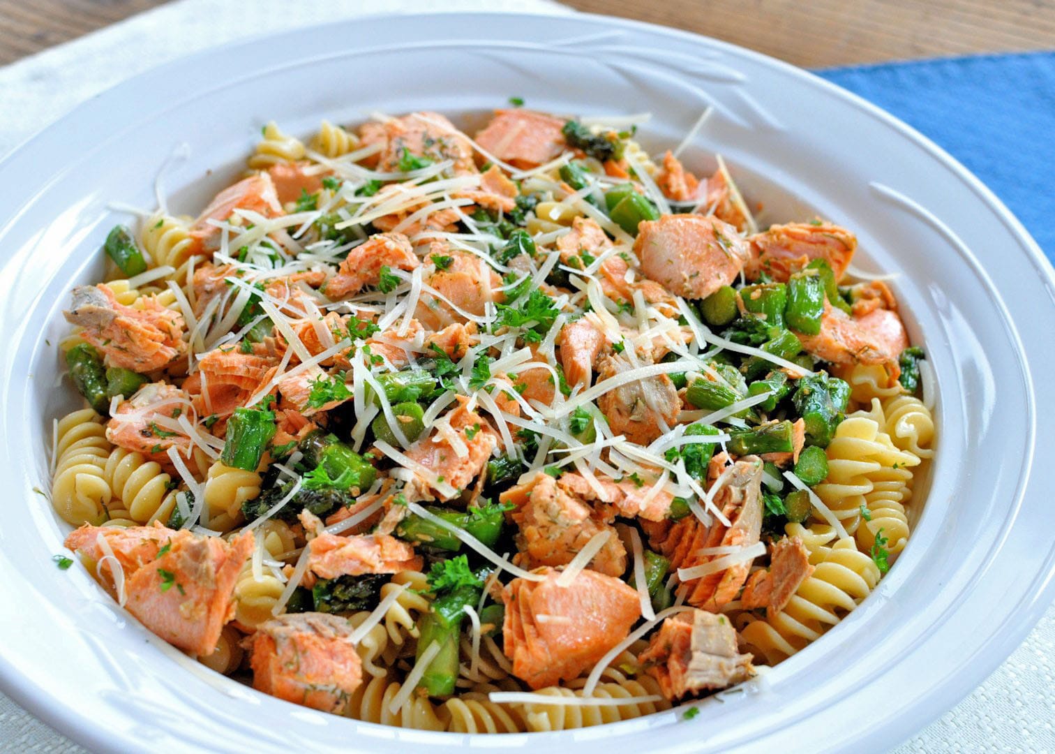 white bowl filled with spiral pasta, salmon and asparagus