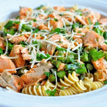salmon crumbled with pasta and asparagus in a white bowl