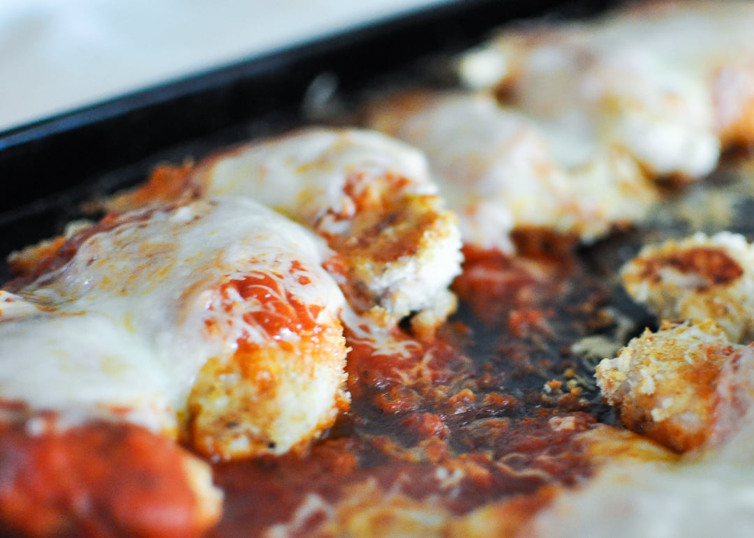 chicken with bread coating, tomato sauce and cheese on a baking sheet