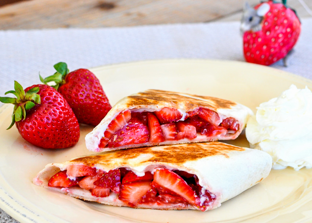 Strawberry Burritos next to whipped cream sitting on a plate