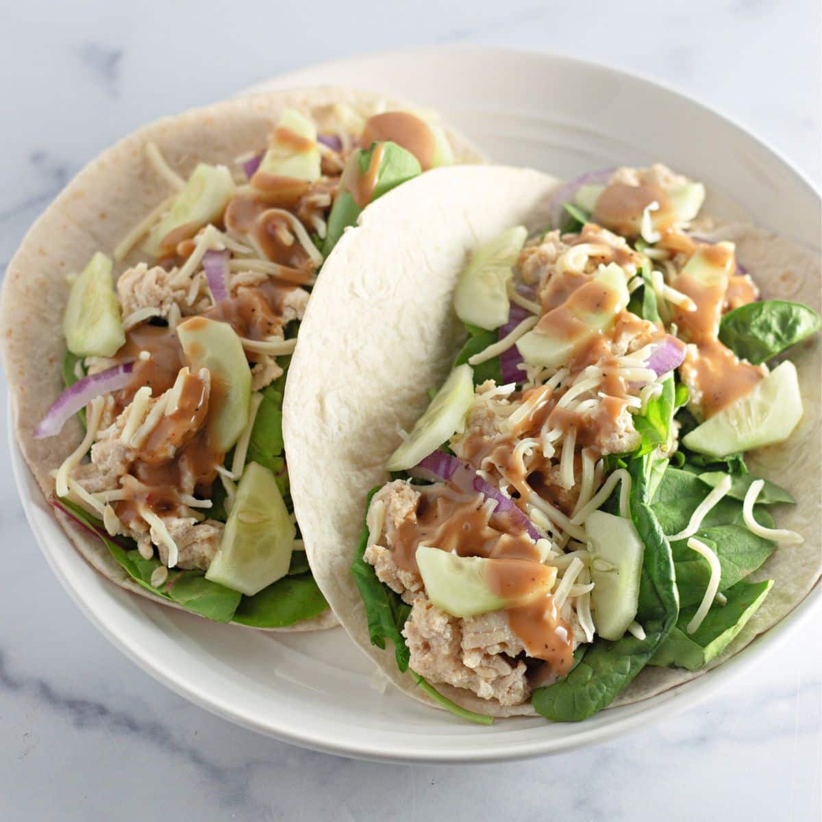 Chicken Sesame Ginger Wraps, feature shredded chicken, spinach, cucumber, cheese, and sauce on a white plate.