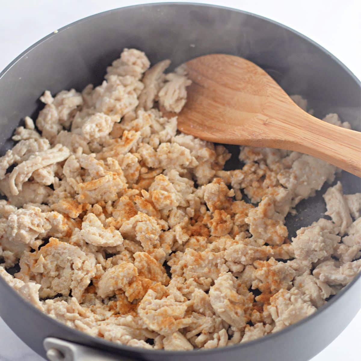Cooked ground turkey with spices in a skillet, stirred with a wooden spoon-perfect for filling Chicken Sesame Ginger Wraps.