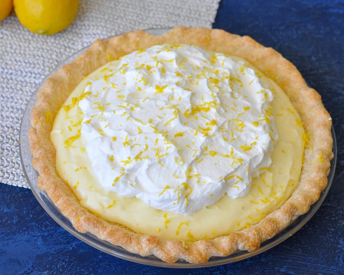 a whole lemon cream pie next to lemons on a blue background