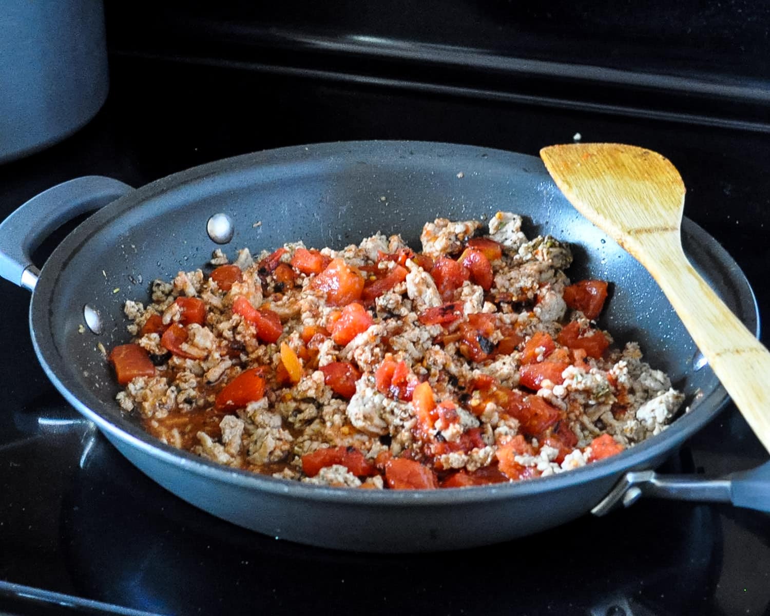 ground turkey and spices with tomatoes cooking in a skillet