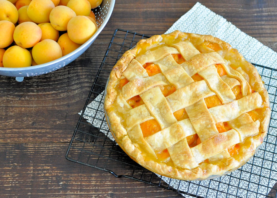 a fresh baked pie sitting next to a bowl of fresh apricots