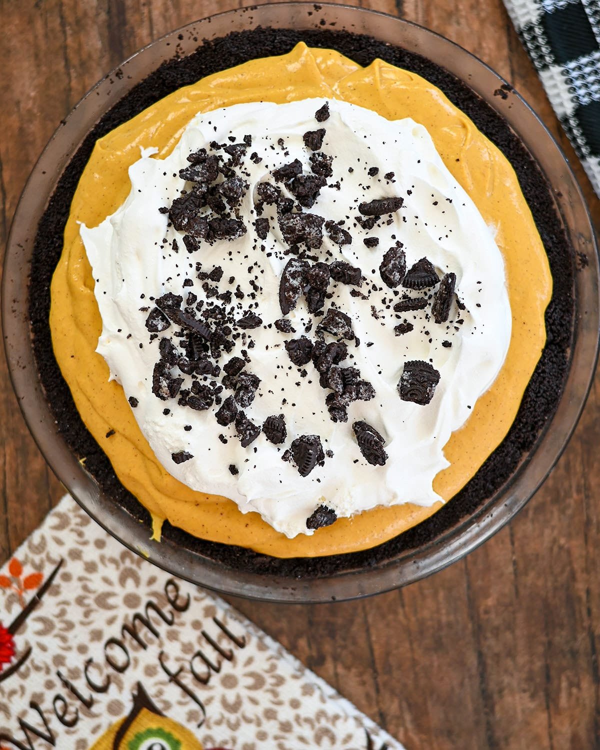 Pumpkin cream cheese filling pie in a oreo crust next to an autumn themed towel. 