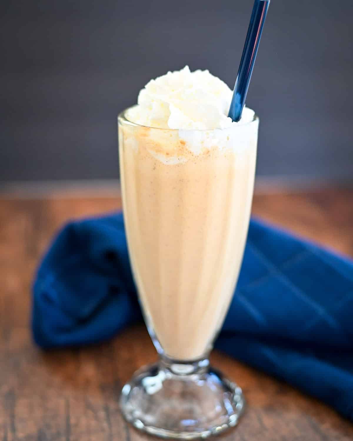 Pumpkin Milkshake in a glass with a blue straw next to a blue towel.