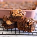 Three chocolate brownies with peanut butter swirls stacked on a wire rack, reminiscent of Nutter Butter Chocolate Chip Brownies, with a baking tray in the background.