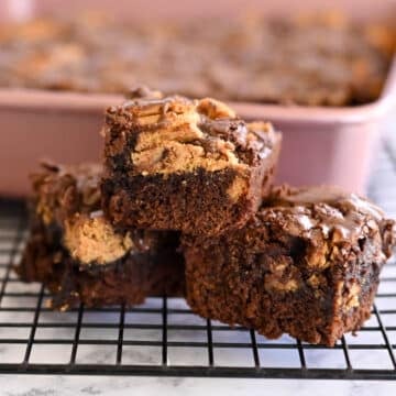 Three chocolate brownies with peanut butter swirls stacked on a wire rack, reminiscent of Nutter Butter Chocolate Chip Brownies, with a baking tray in the background.
