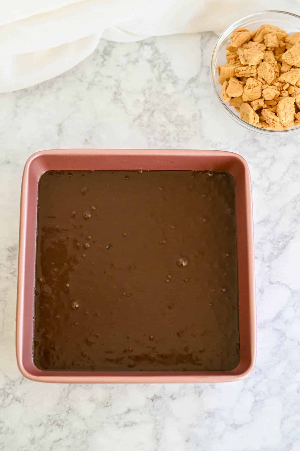 Brownie batter in a square baking pan on a marble surface.