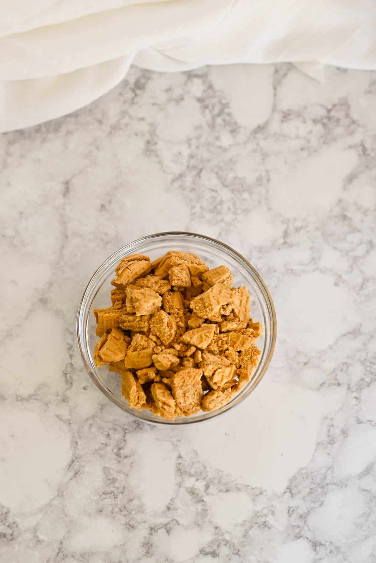 A bowl of crumbled Nutter Butter cookies rests on a marble surface,.