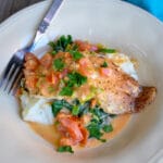 Pan-seared Tilapia with a Creamy Tomato Sauce over bacon mashed potatoes and greens, garnished with parsley and fresh spinach.