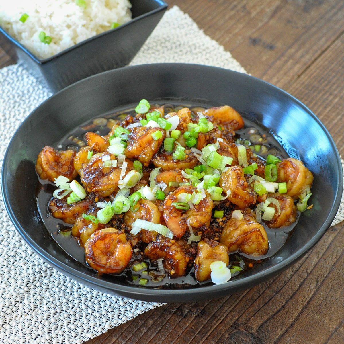 shrimp with a sweet garlic sauce in a black bowl topped with green onions