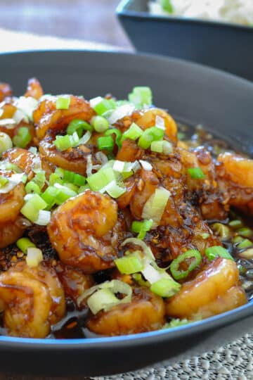 shrimp with a sweet garlic sauce in a black bowl topped with green onions