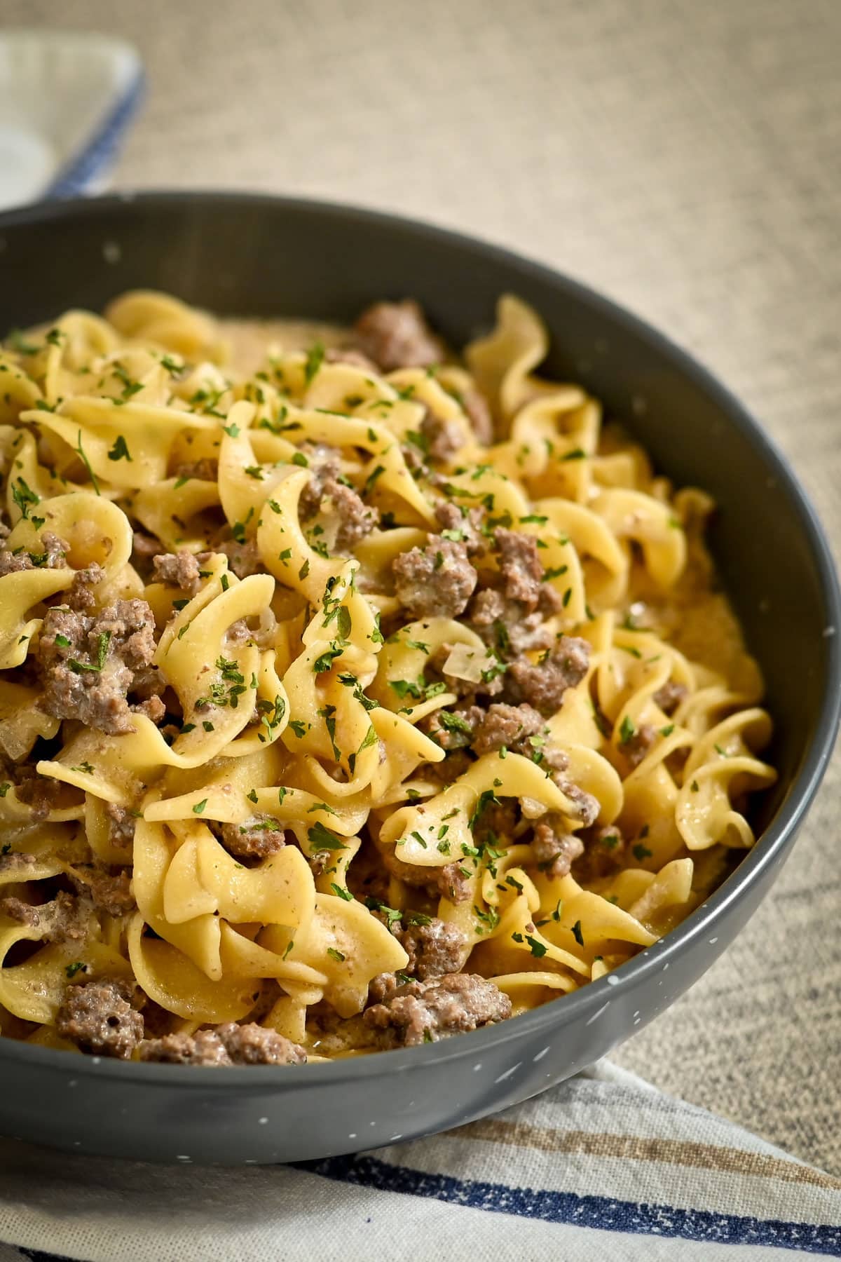 A bowl of egg noodles mixed with ground beef, inspired by a classic Simple Hamburger Stroganoff, and garnished with chopped parsley.
