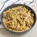 A bowl of creamy ground beef stroganoff with egg noodles, topped with chopped parsley, on a textured surface. This simple hamburger stroganoff makes for a comforting and delicious meal.
