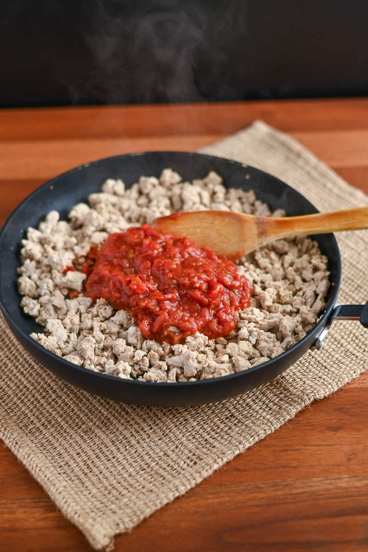 A skillet with cooked ground meat and tomato sauce for Taco Sloppy Joes recipes is being stirred with a wooden spoon.