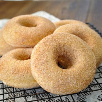 a stack of cinnamon sugar covered baked donuts on a black wire rack