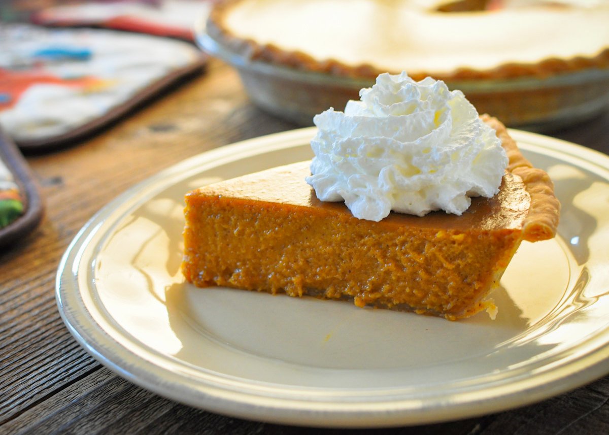 a slice of fresh butternut squash pie topped with whipped cream on a cream colored plate