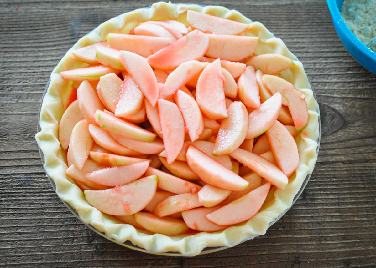sliced apples covered in red hot candy sauce poured into a pie shell