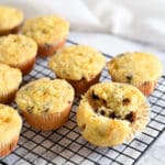 Chocolate Chip Orange Muffins cooling on a wire rack, with a hint of fresh oranges. One muffin is broken in half.