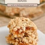 Two oatmeal apricot bars stacked on white paper, reminiscent of classic Apricot Oatmeal Bars, with a baking dish of bars in the background.