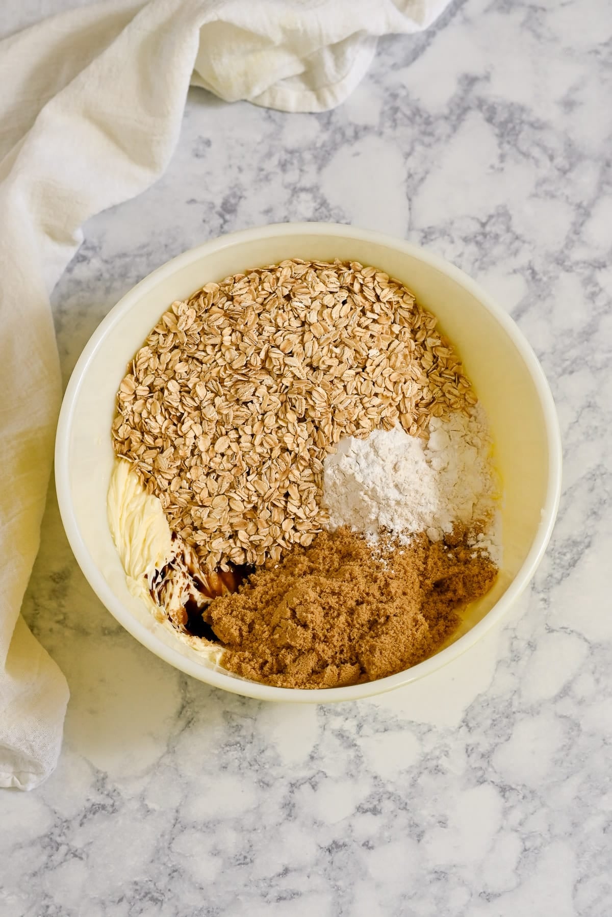 Mixing bowl with oats, flour, brown sugar, and butter on a marble countertop-perfect for preparing delicious Apricot Bars-cloth beside the bowl.