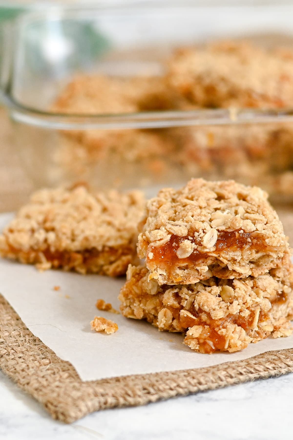 Two Apricot Bars stacked on parchment paper, with a glass baking dish in the background.