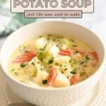 A bowl of homemade potato soup with carrots and celery sits on a plate, with a spoon beside it, ready to enjoy.