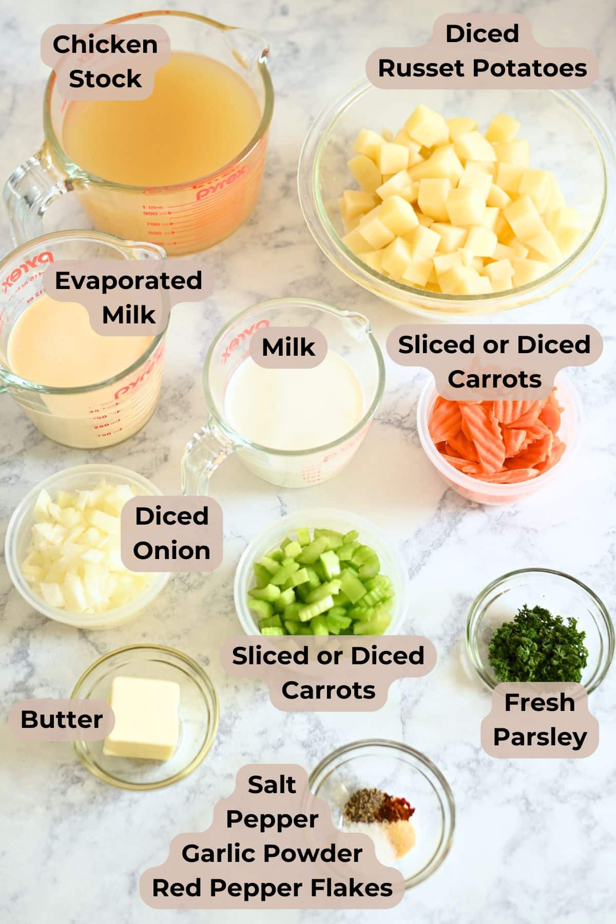 Various bowls with labeled soup ingredients for homemade potato soup: potatoes, chicken stock, milk, carrots, onion, celery, butter, and seasonings.