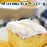 A piece of lemonade cake topped with marshmallow frosting is on a plate next to a lemon slice. The cake's light and fluffy texture is visible. "Lemonade Cake with Marshmallow Frosting" text highlights the delectable dessert in the image.