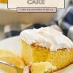 A slice of Lemonade Cake Marshmallow Frosting, topped with fluffy marshmallow frosting and served with fresh lemon slices on a white plate.