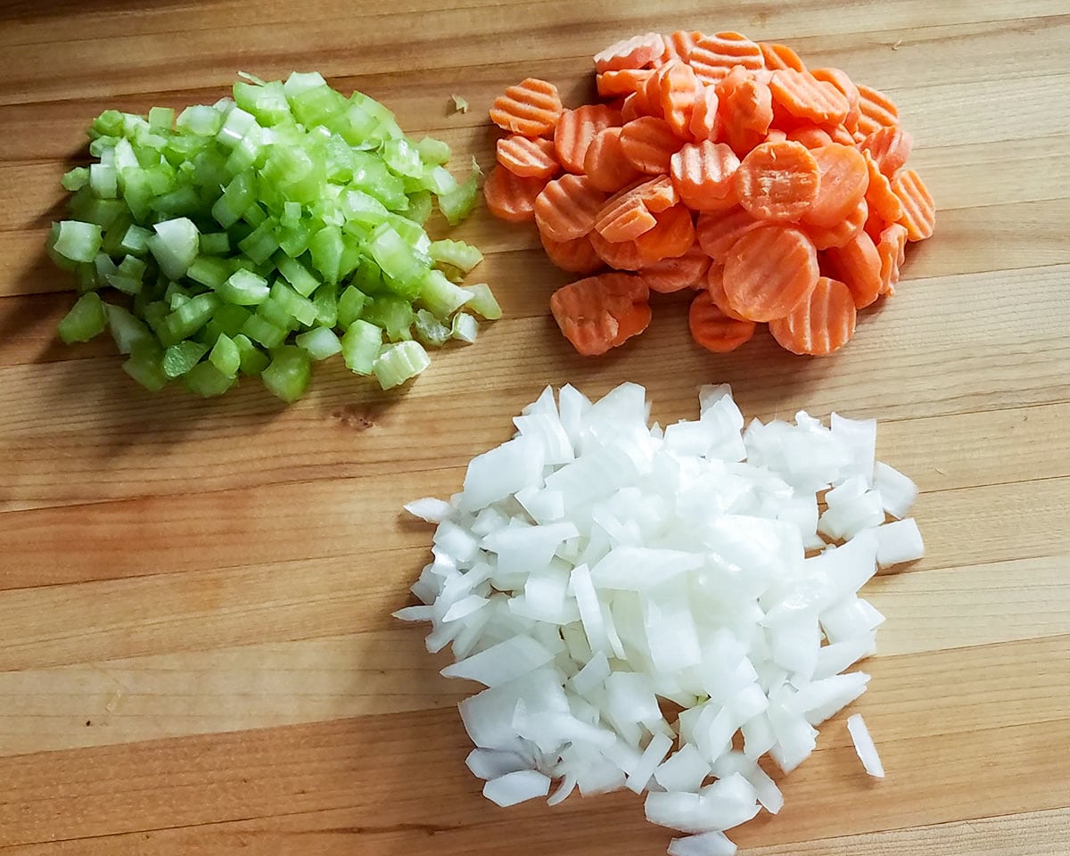diced celery, carrots, and onion in separate piles on a wood cutting board