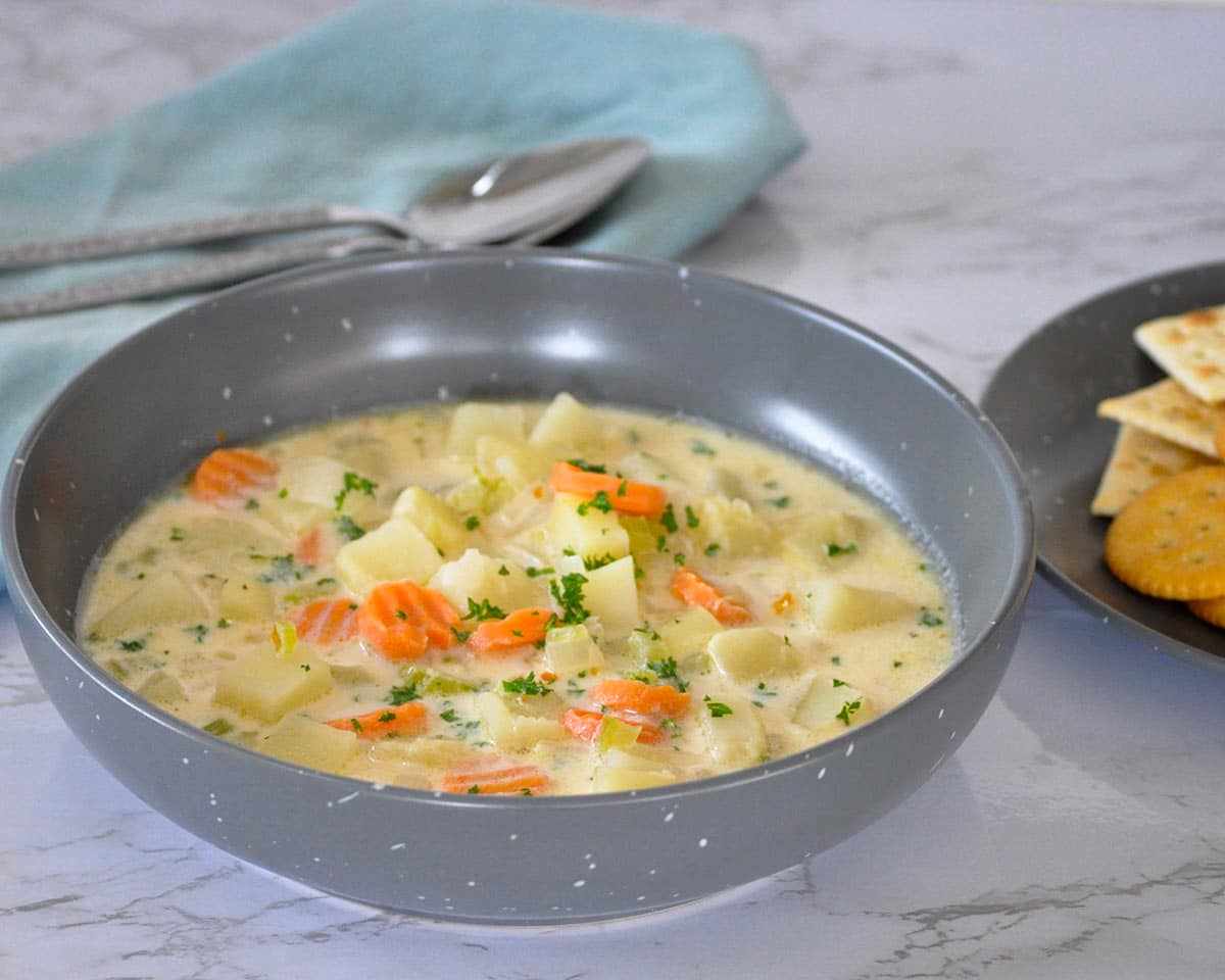 gray bowl of potato soup sitting next to a plate of crackers