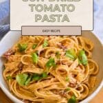 A bowl of creamy sun-dried tomato pasta made with smooth cream cheese, garnished with fresh basil leaves on a wooden table.