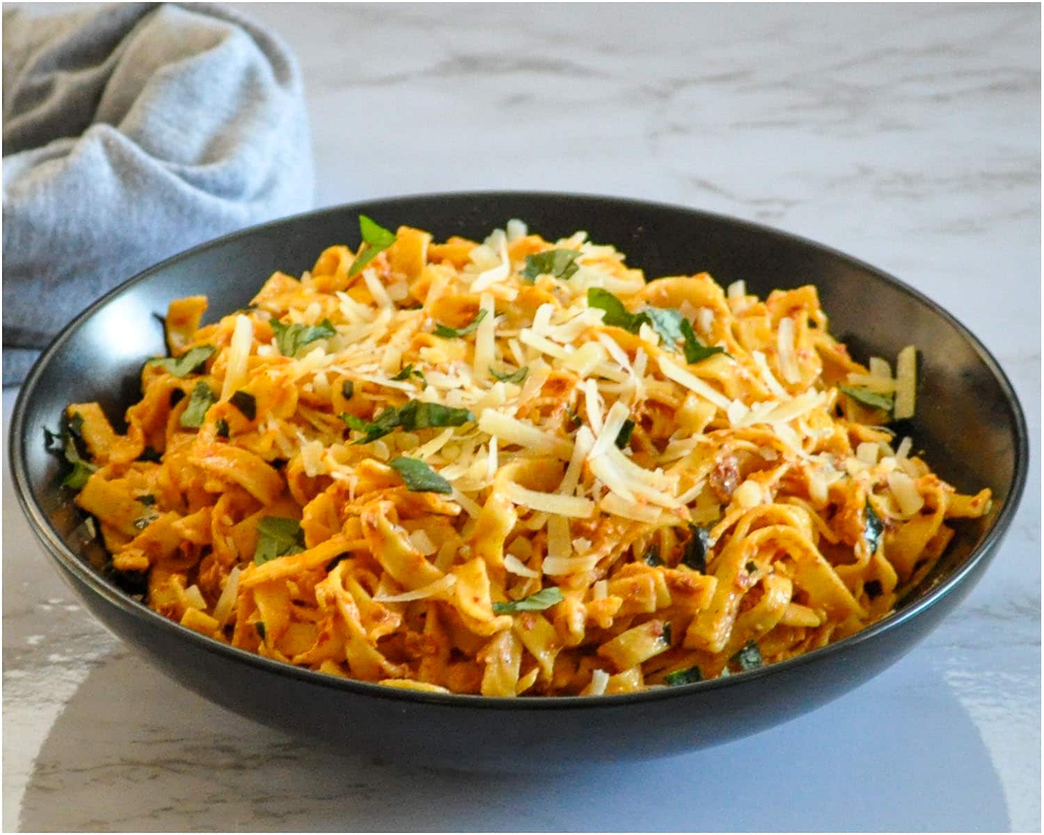 a black bowl with pasta and creamy tomato sauce