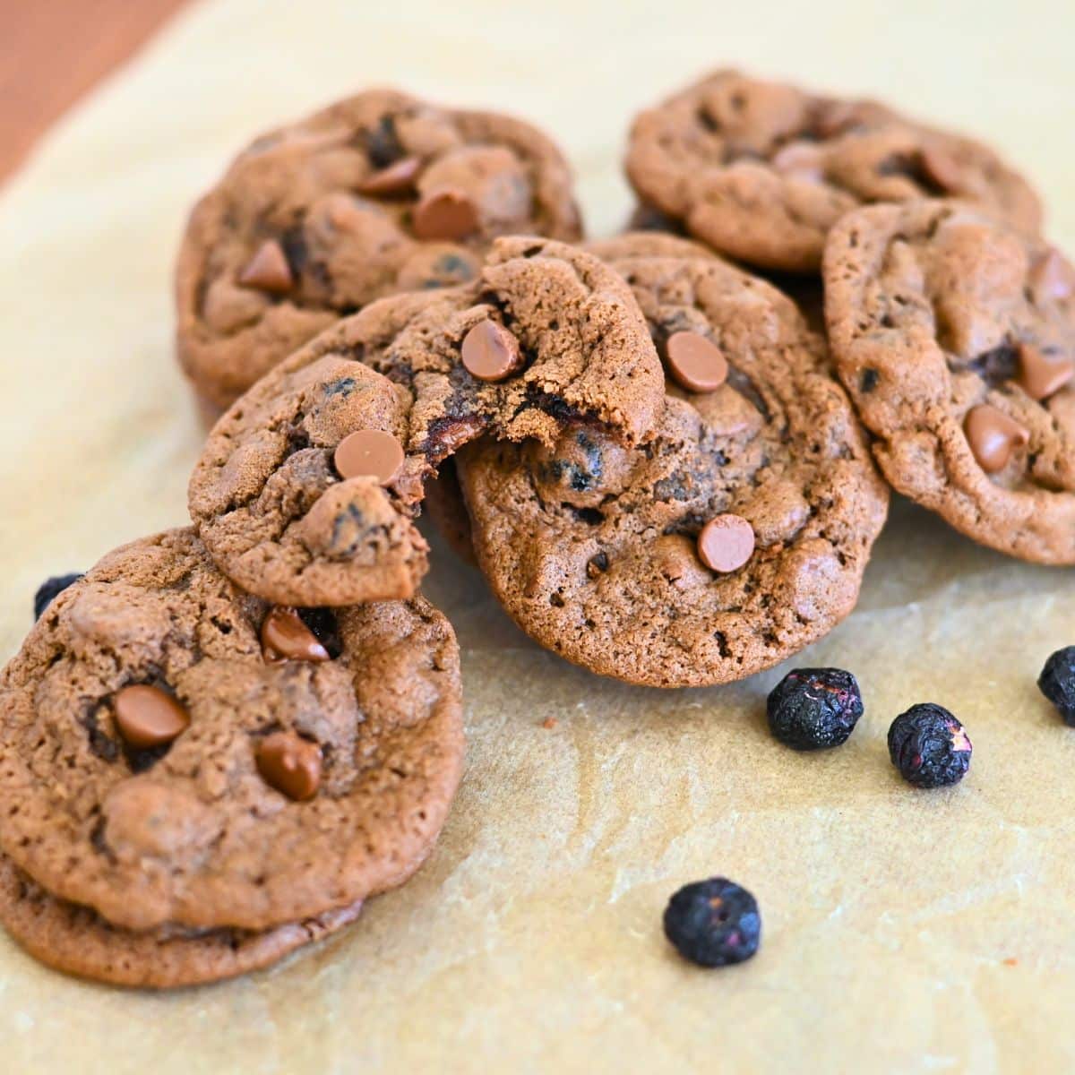 Blueberry Chocolate Chip Cookies on parchment paper. One cookie is broken in half, displaying its soft interior.