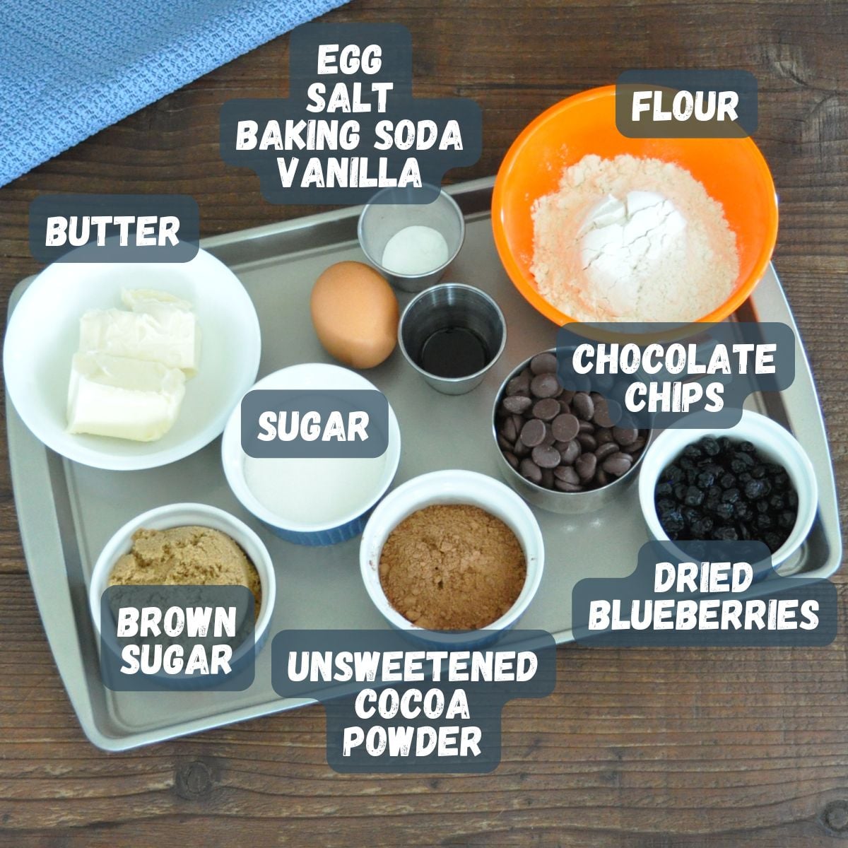 Baking ingredients on a tray, each labeled: flour, butter, brown sugar, egg, and more-everything you need to make delicious Blueberry Chocolate Chip Cookies.