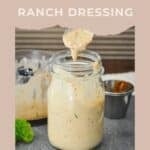 Glass jar of chipotle ranch dressing with a spoon, set on a table with greenery and a mixing bowl nearby—perfect for adding bold flavor to any dish with this creamy Chipotle Ranch Sauce.