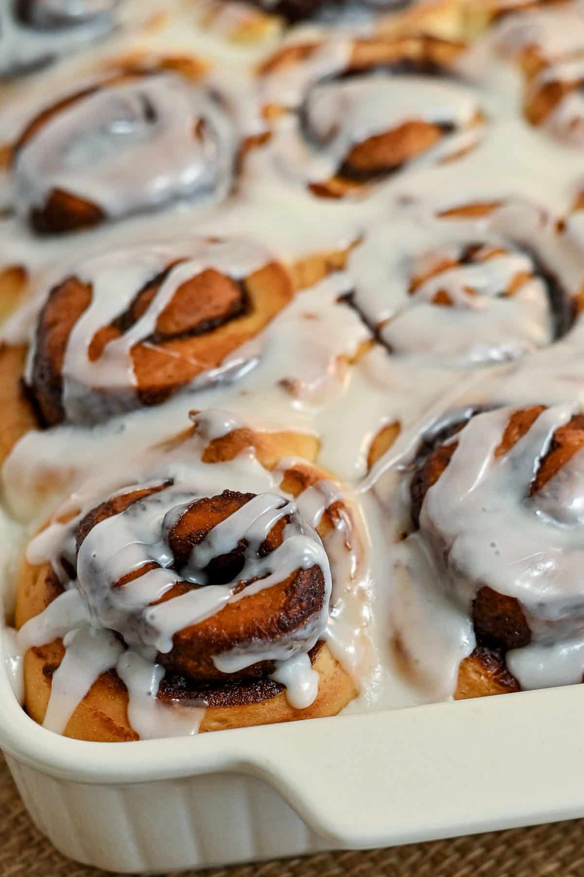 Close-up of freshly baked chocolate cinnamon rolls in a dish, topped with melted white icing.