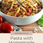 A white bowl of Homemade Turkey Sausage Pasta with fresh tomatoes, garnished with cheese, on a wooden table.